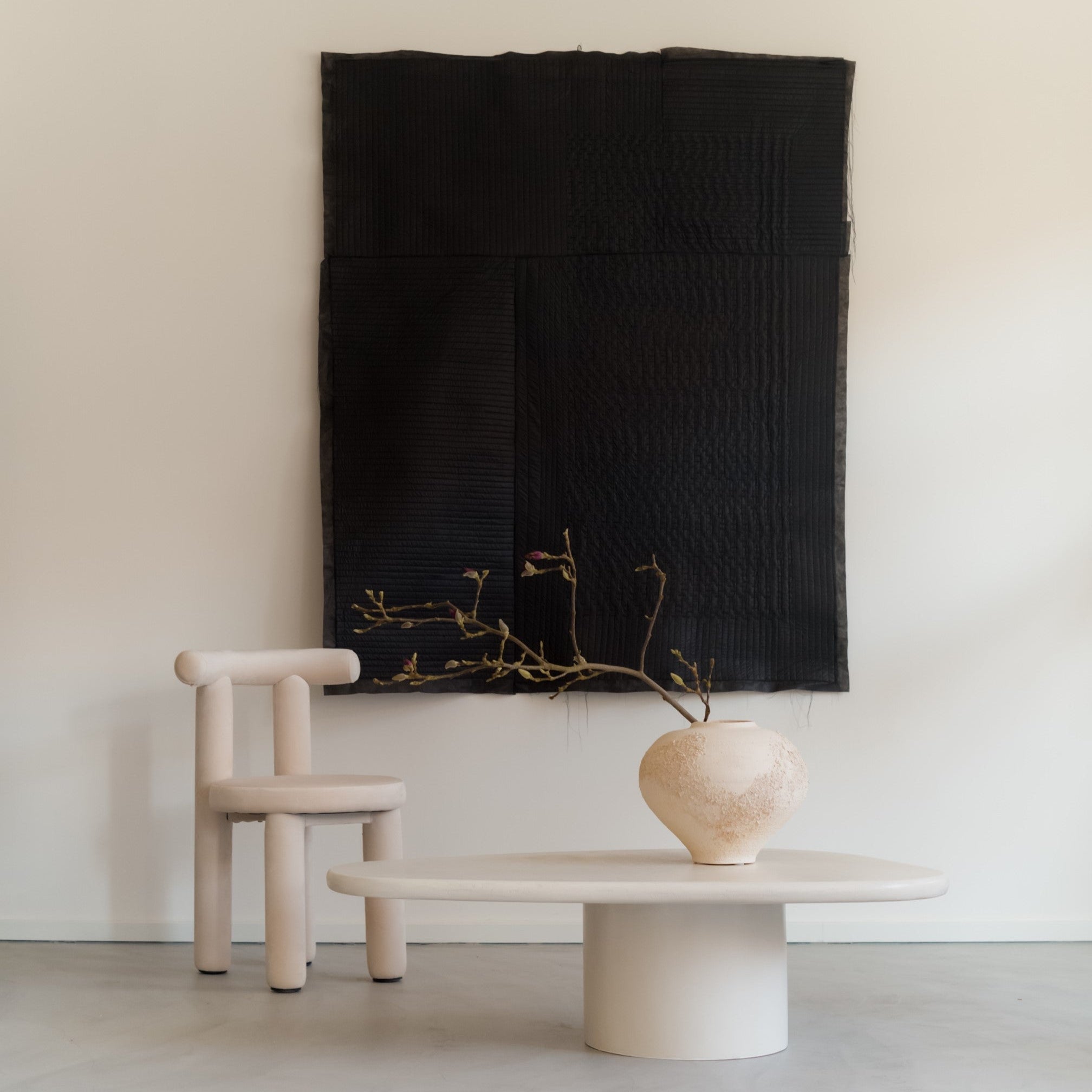 Kanso Wing microcement coffee table styled in minimalist interior with chair and wall textile