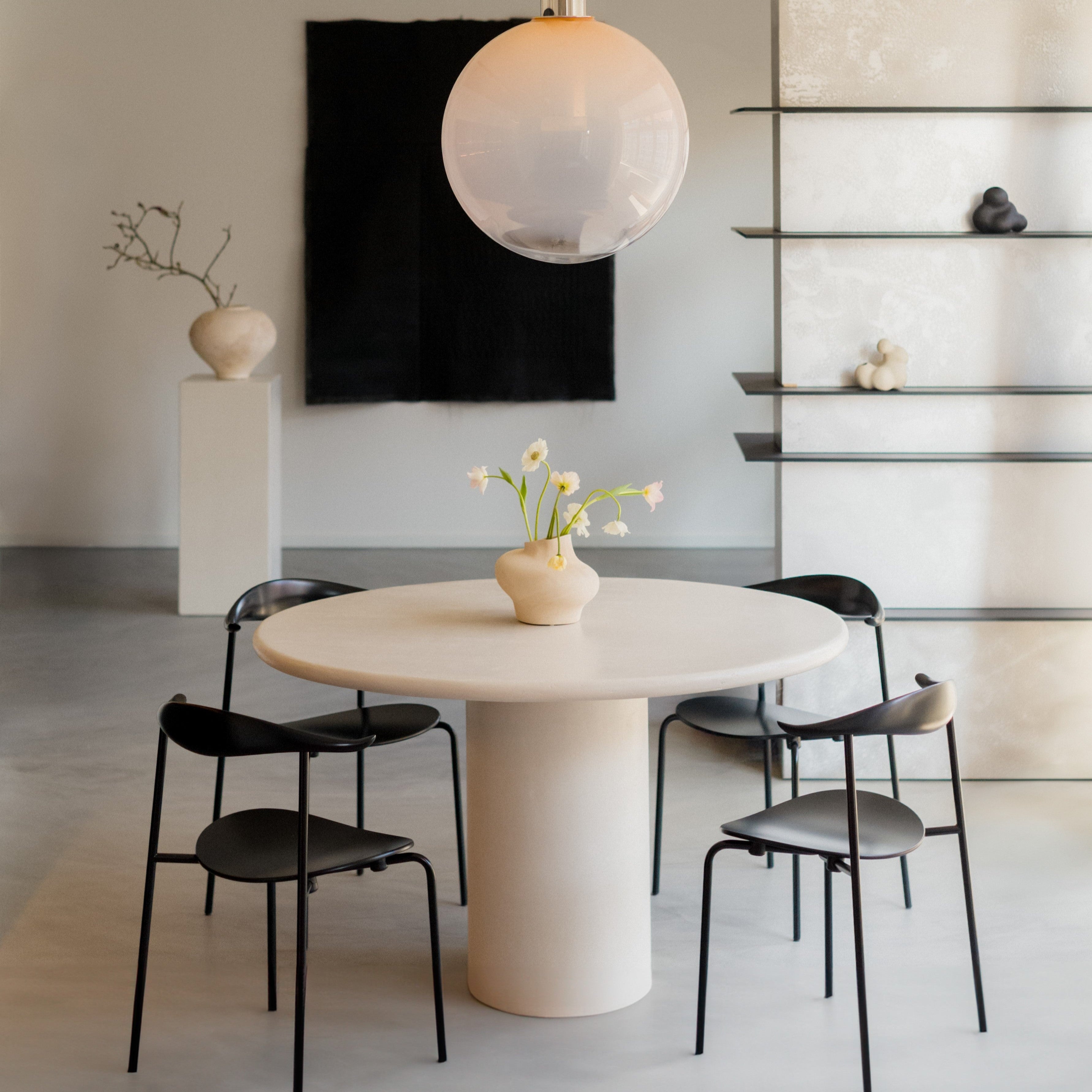 Kanso Round microcement dining table styled with black chairs and pendant lamp