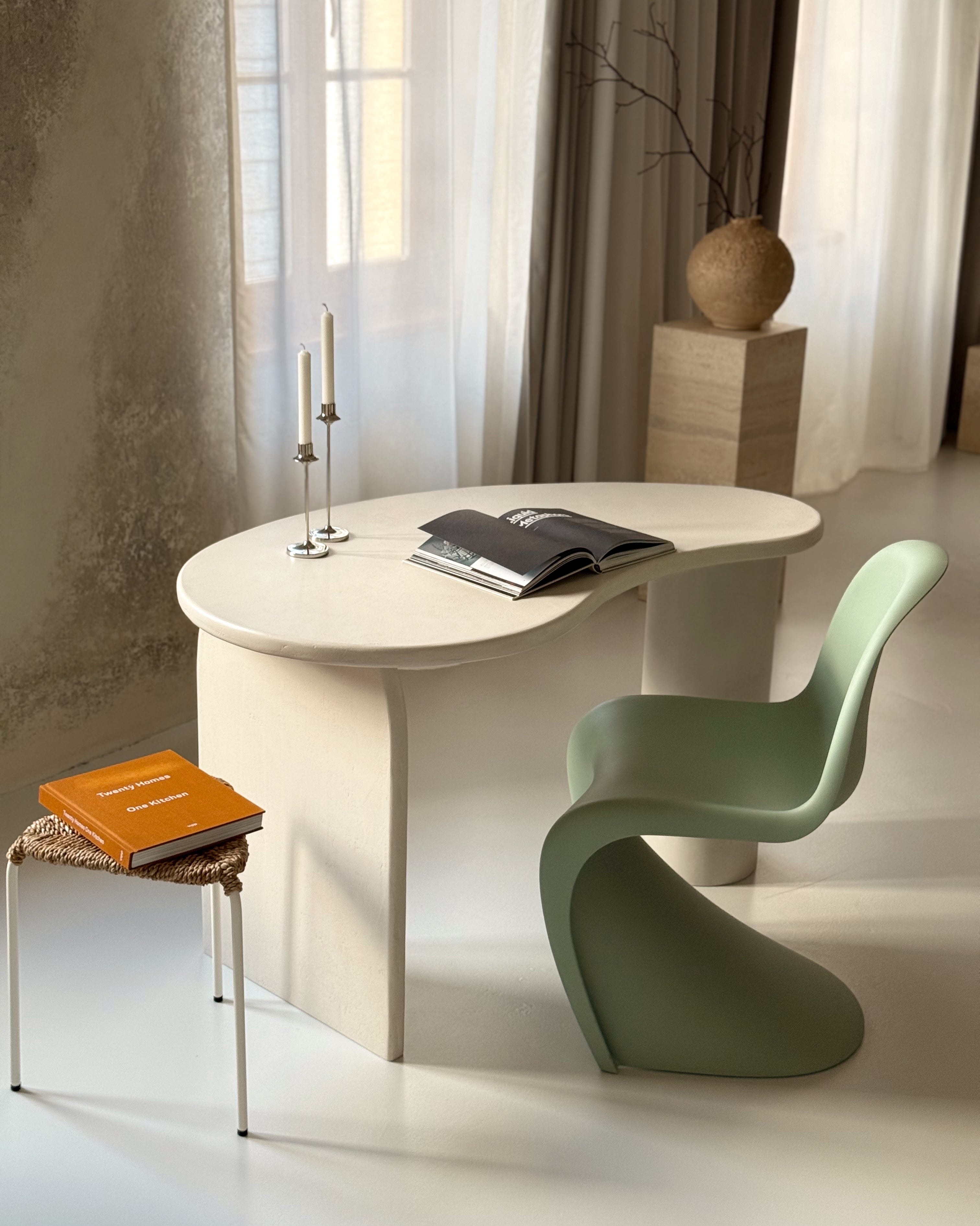 Kanso kidney-shaped microcement desk styled with green chair and magazine in modern interior
