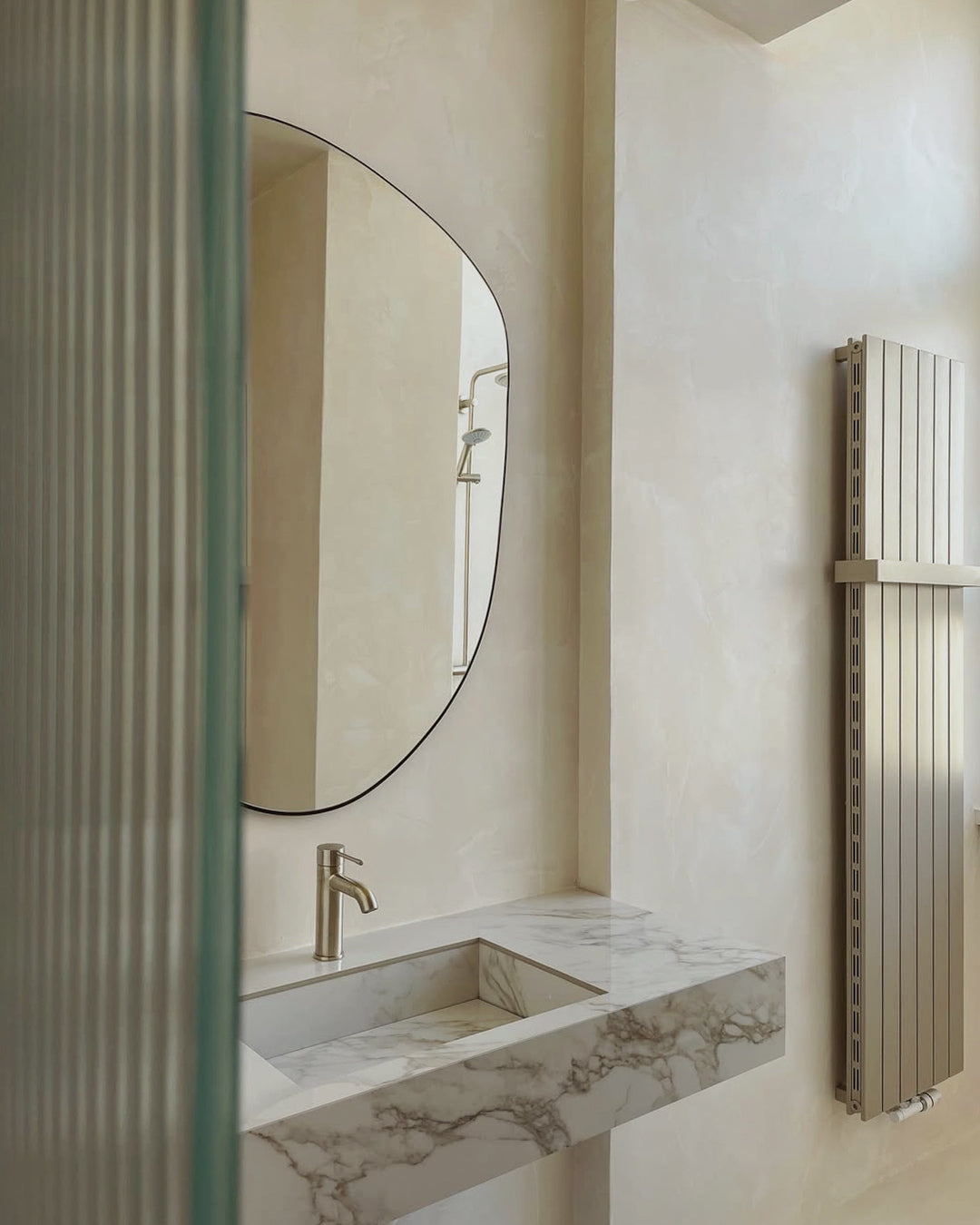 Minimalist bathroom with microcement walls and a marble sink, featuring modern brass fixtures and a neutral color palette.