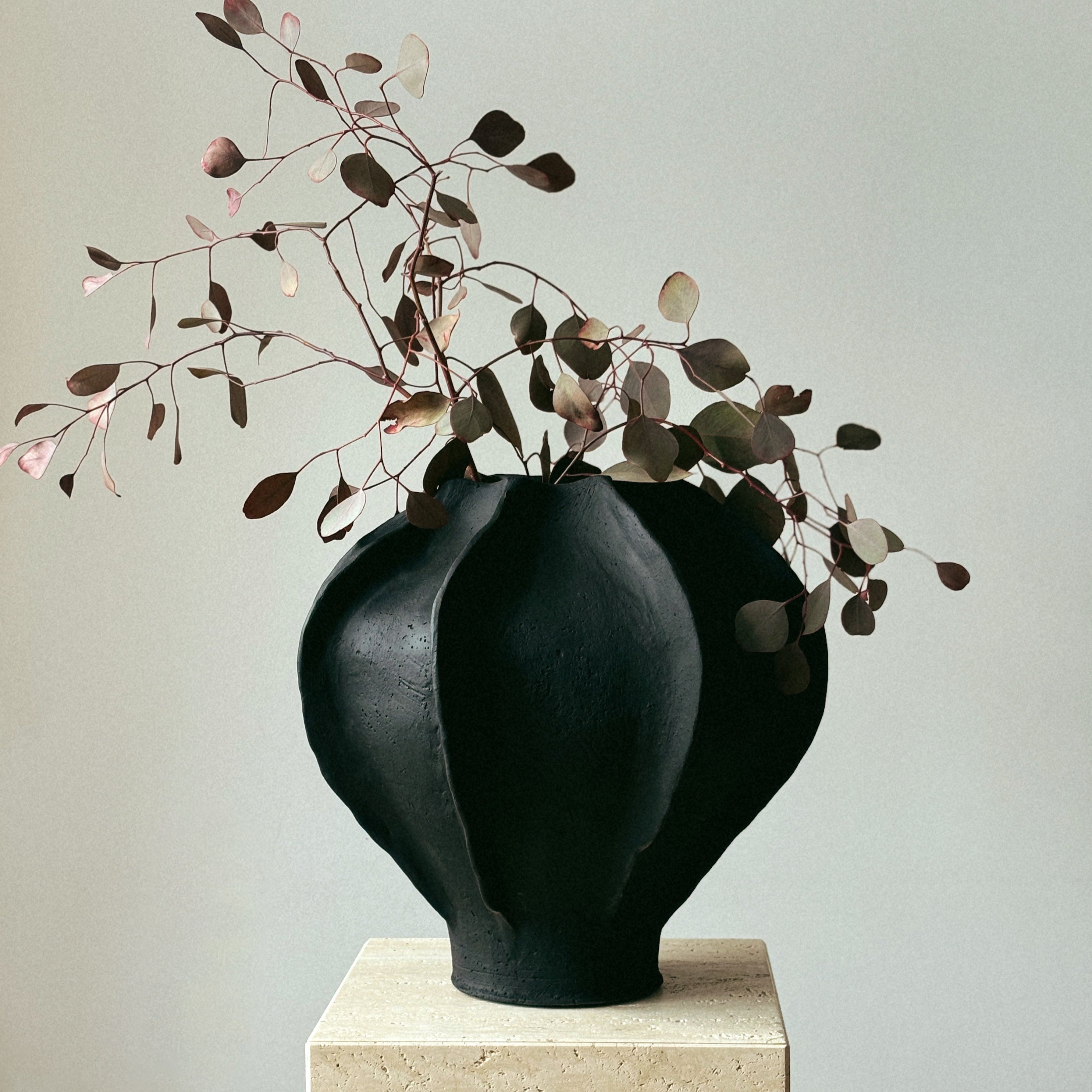 Large handmade black ceramic Sabi vase styled with dried branches on travertine pedestal