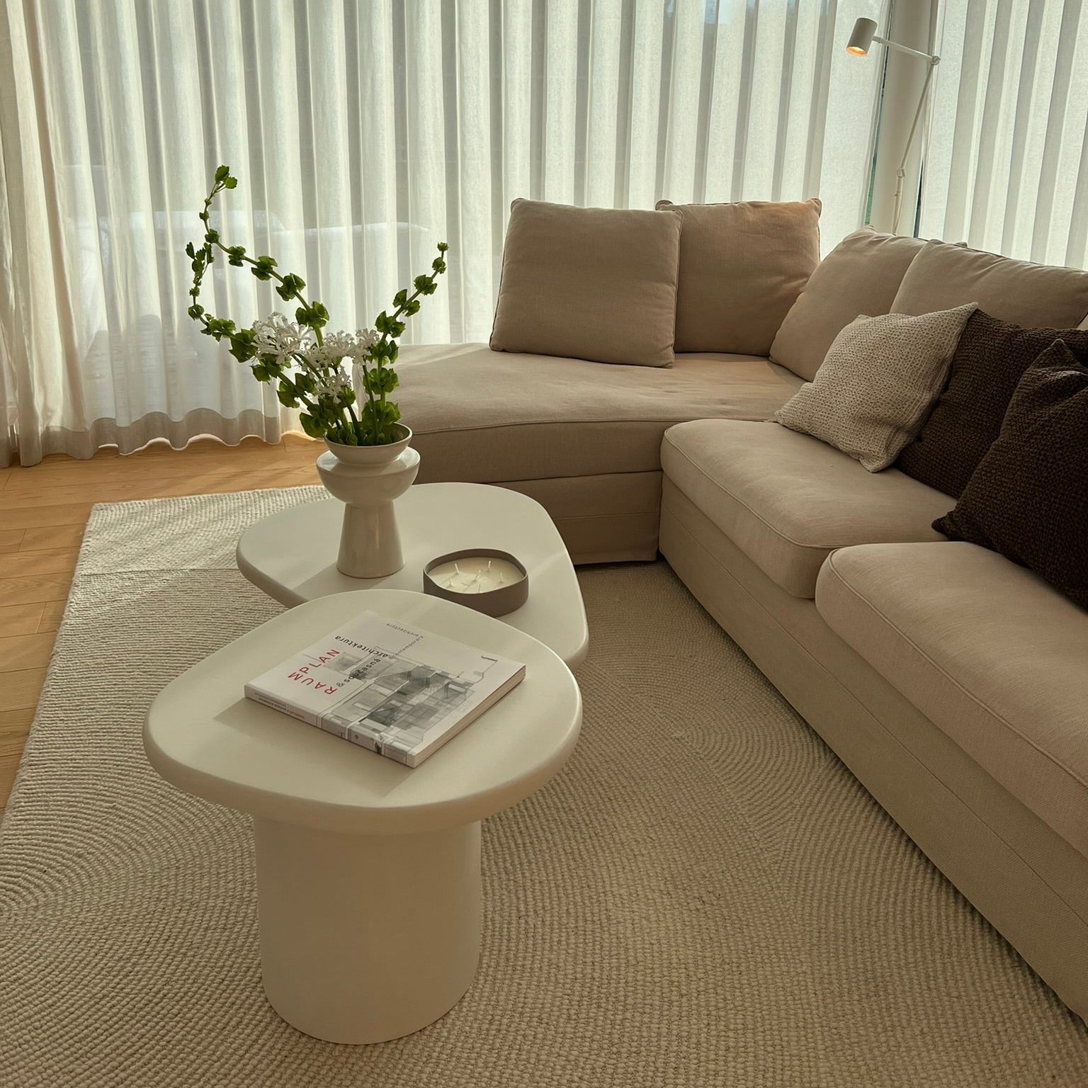 Two Kanso microcement set in organic form in a warm living room with beige sofa, neutral rug, and natural daylight.