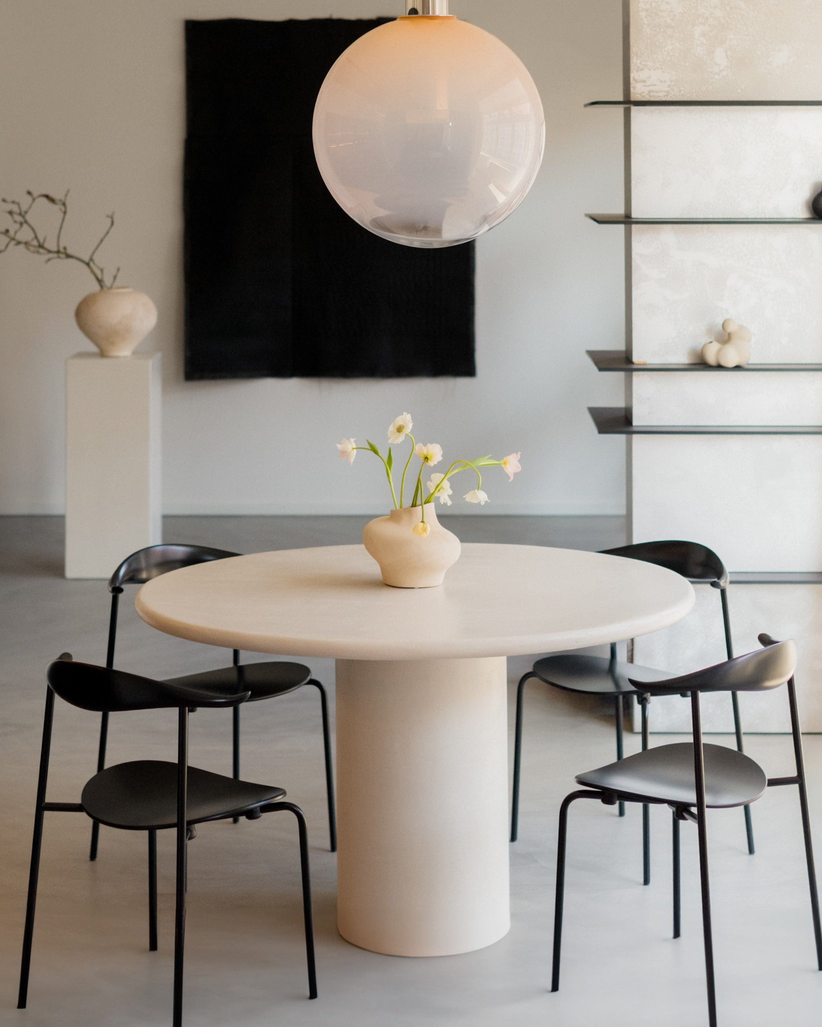 Kanso Round microcement dining table styled with black chairs and pendant lamp