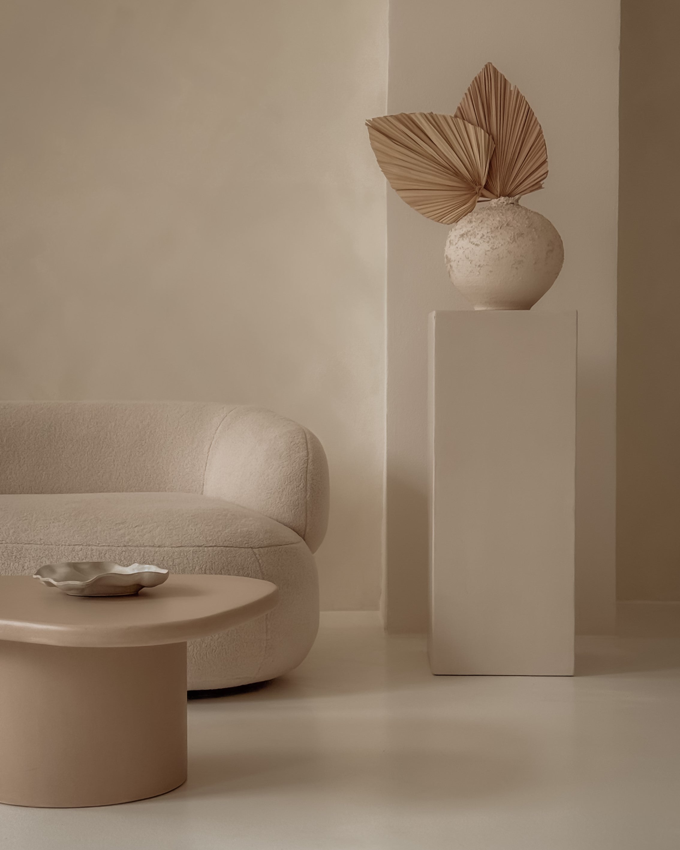 Tall microcement pedestal with smooth sculptural surface, styled with natural decor