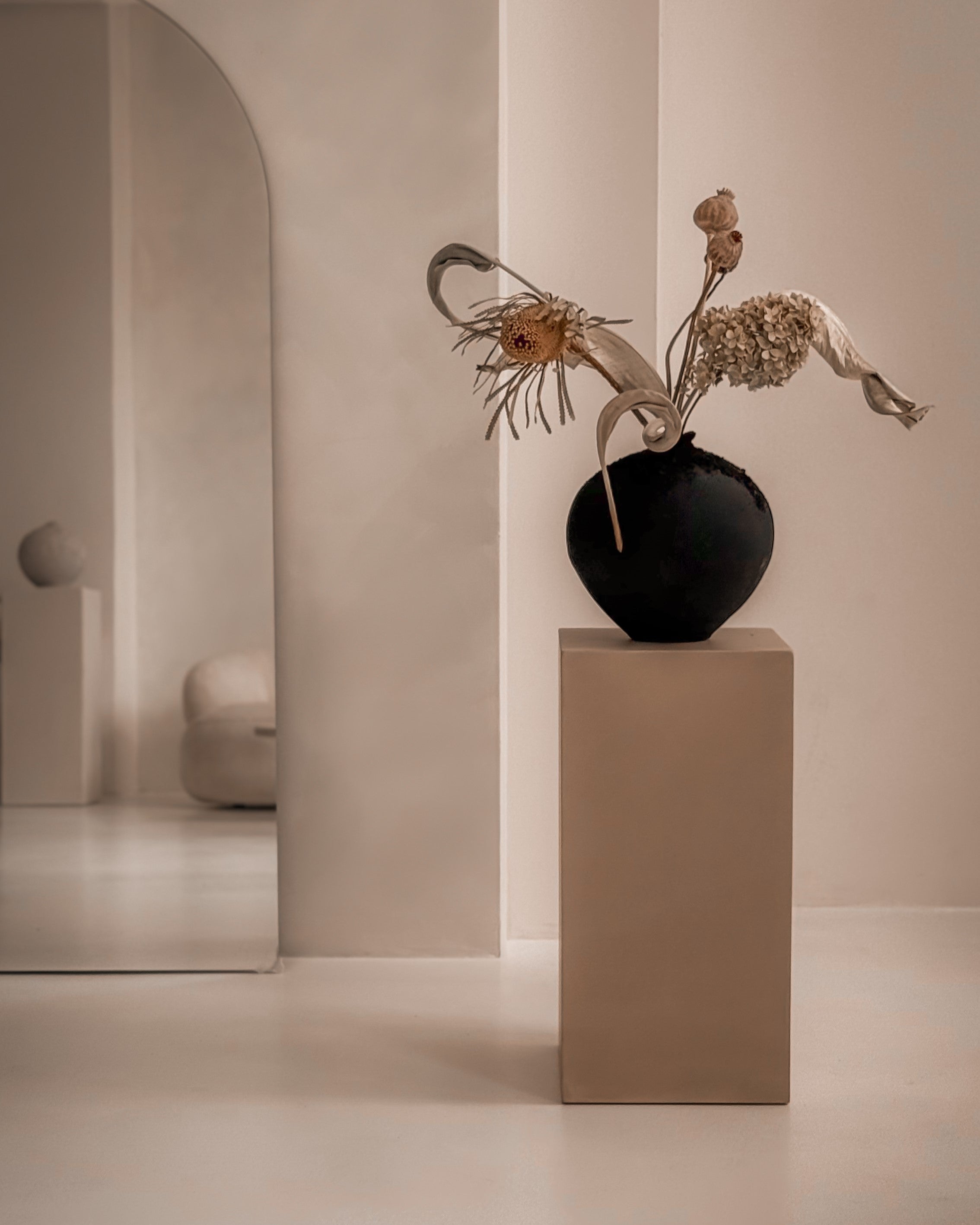 Microcement pedestal styled with black ceramic vase, minimalist interior setting