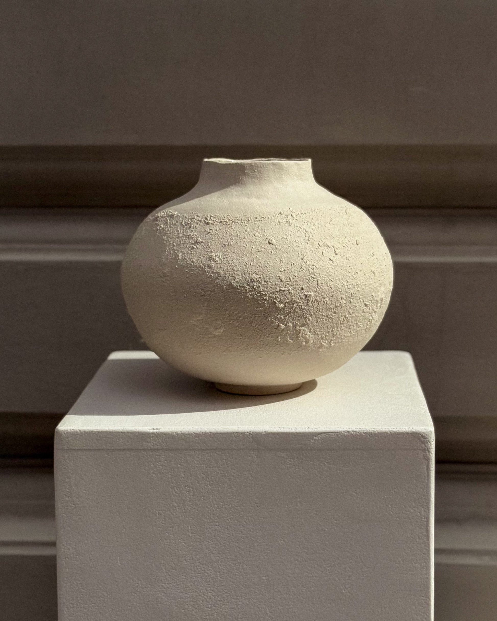 Minimalist stoneware vase displayed on a pedestal – refined, timeless design for modern interiors.
