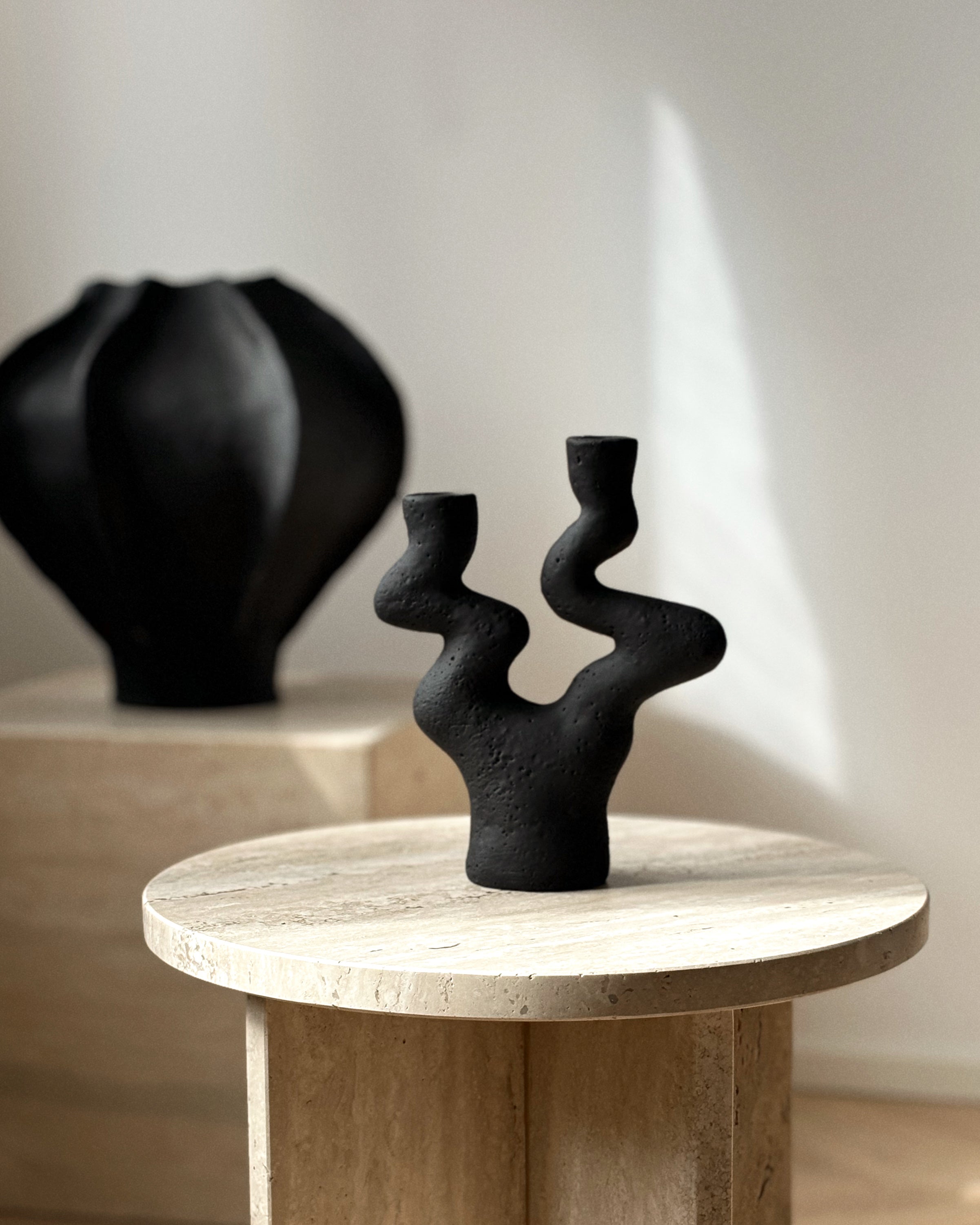 Sabi handcrafted black ceramic candle holder styled on wooden table with vase in background